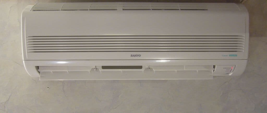 Technicien souriant qui met en service une thermopompe murale dans un salon lumineux