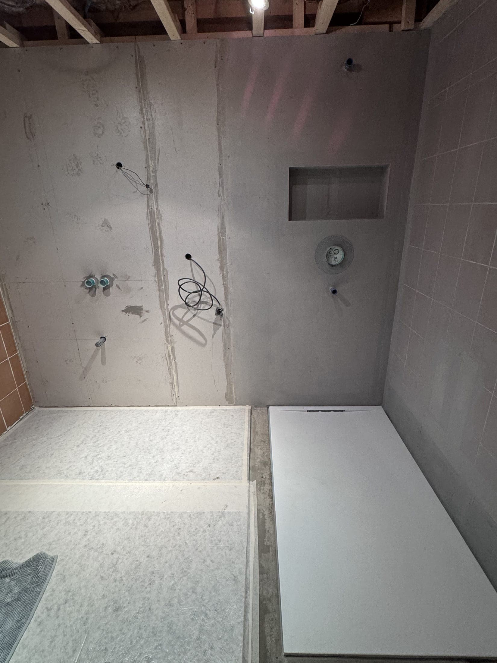 Salle de bain en travaux : receveur de douche rectangulaire blanc posé dans l'angle, attentes d'eau et niche de rangement.