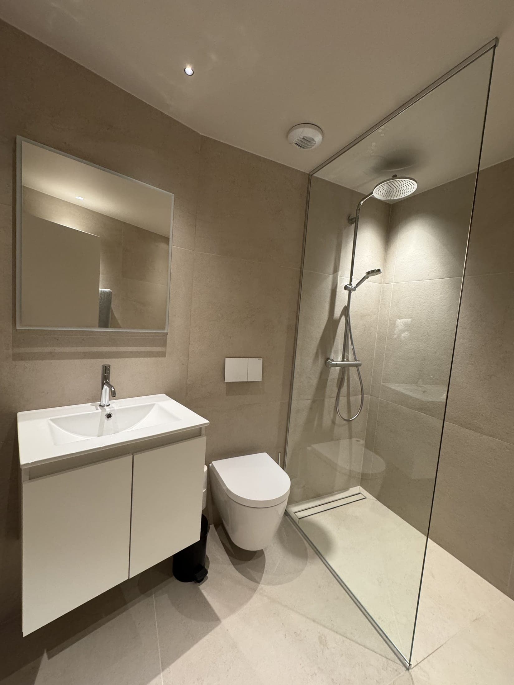Vue d'ensemble : meuble vasque blanc suspendu avec miroir, WC suspendu et douche à l'italienne vitrée.
