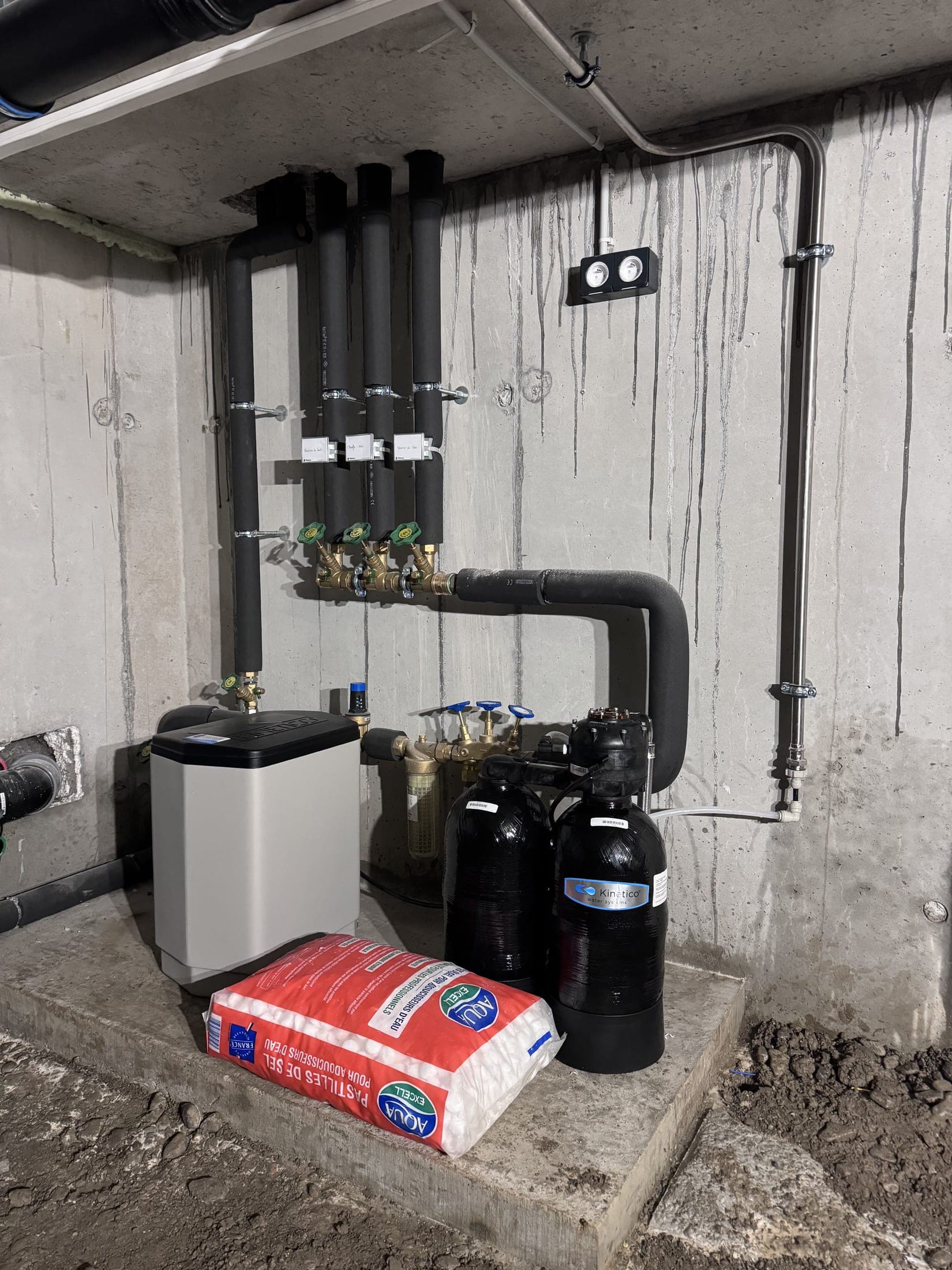 Local technique : bac à sel blanc, deux bouteilles de traitement noires et collecteur en laiton à vannes.